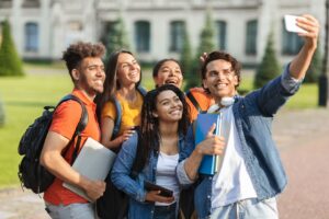 Portrait of happy multiethnic students talking selfie on smartphone outdoors